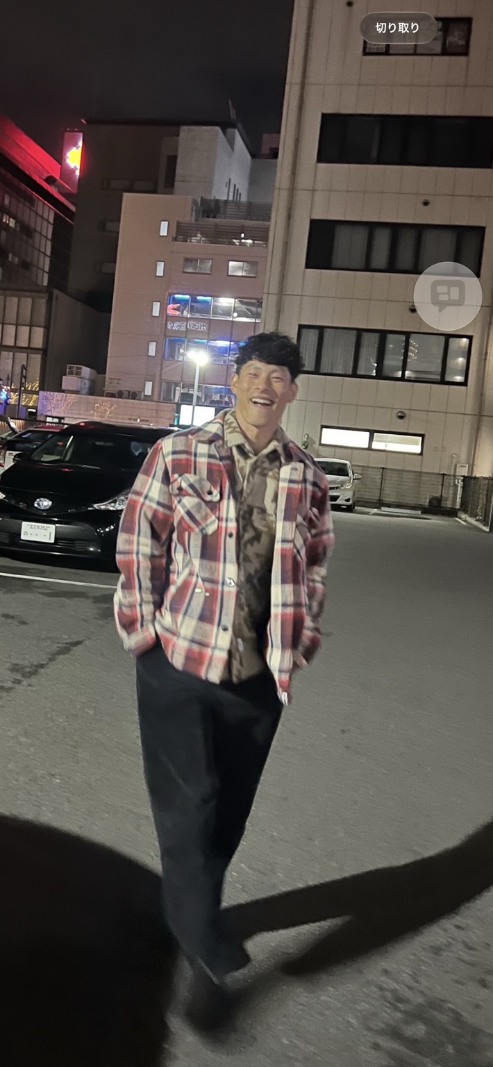 チェック柄のシャツを着て、屋外で笑顔を見せる竹下真吾さん